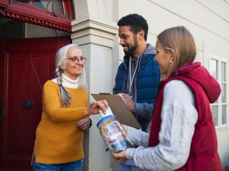 young-door-to-door-fundraisers-talking-to-senior-woman-and-collecting-money-for-charity-in-street.jpg